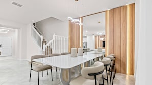Et moderne spiseområde med et langt hvidt bord, beige stole og en trævæg.