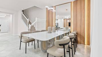 A modern dining area with a long white table, beige chairs, and a wooden accent wall.