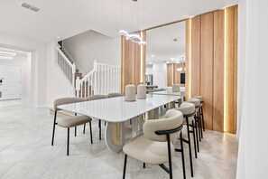Ein moderner Essbereich mit einem langen weißen Tisch, beigen Stühlen und einer Wand aus Holz.
