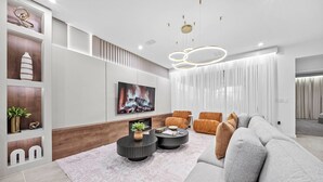 Una sala de estar moderna con un sofá gris, dos mesas de centro negras y redondas, un televisor montado en la pared y una chimenea.