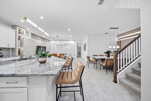 A modern kitchen with a marble countertop, built-in cabinets, and a central island with bar stools. - 7BR house with private pool near Disney (Kissimmee)