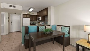 Una cocina moderna con armarios de madera oscura, un refrigerador blanco y un microondas. Hay una mesa de comedor con un centro de mesa con planta y cojines azul verdoso.