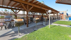 Un patio al aire libre con mesas de madera y parrillas, rodeado por una valla de madera.