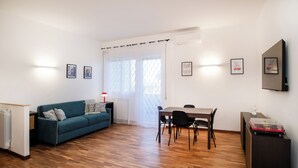 Una sala de estar moderna con un sofá azul, piso de madera, una mesa de comedor con sillas y cuadros en las paredes.