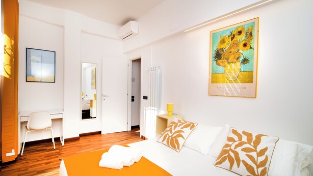 Habitación de hotel con cama, escritorio y silla. Hay un cuadro en la pared y una ventana con cortinas.