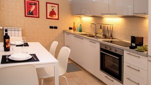 Una cocina moderna con armarios blancos, horno empotrado y una zona de comedor con mesa y sillas blancas.