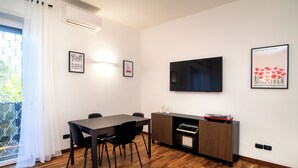 Una sala de estar moderna con piso de madera, una mesa de comedor con sillas, un televisor de pantalla plana montado en la pared y un mueble con un tocadiscos.
