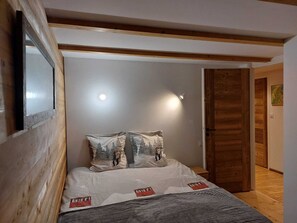 Ein Schlafzimmer mit Bett, Nachttisch, Holztür und Wandleuchte.