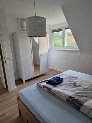 Une chambre à coucher comprenant un lit, une armoire, un luminaire suspendu et une fenêtre donnant sur un paysage agréable.