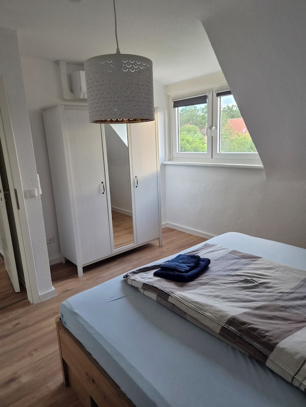 Quarto com cama, guarda-roupa, luminária pendente e janela com vista.