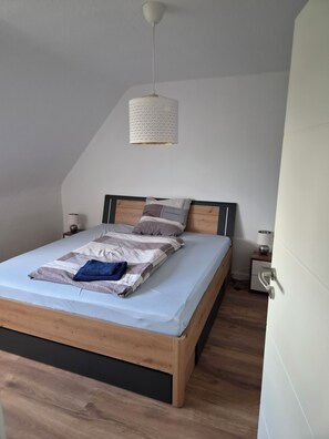 Et soveværelse med en træseng, en hængende lampe, et sengebord med lampe og en dør.