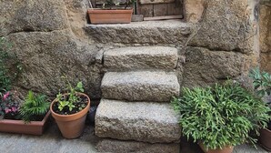 Ein rustikales Steinhaus mit einer Holztür und Stufen, die zu einer kleinen Veranda führen.