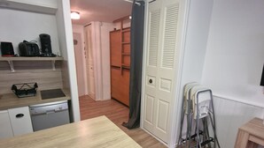 Ett kompakt kök med diskmaskin, kaffebryggare och ett litet kylskåp. Det finns ett träbord och en stol, samt en dörr som leder till en hall.