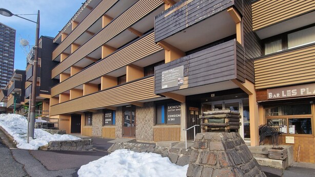 En byggnad med flera våningar och en fasad av sten, ett väl synligt skylt för ”Bar Les Pla”, och en skylt med texten ”Consigne à Ski”, vilket visar att det finns en uthyrning av skidutrustning här.