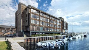 A modern building with a brick facade, large windows, and a dock area with boats.