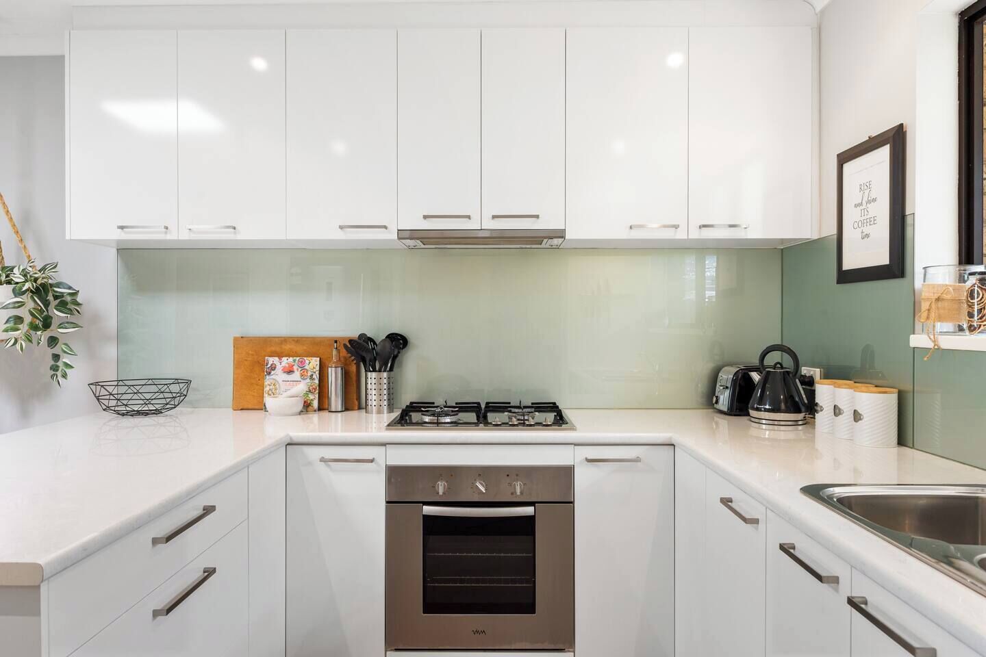 A modern kitchen with white cabinets, a gas stove, an oven, and a stainless steel sink.
