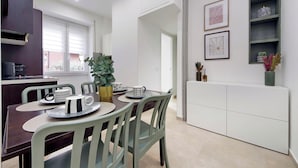 Eine moderne Küche mit weißen Schränken, einem Essbereich mit Tisch und Stühlen sowie ein Blick ins Freie durch ein Fenster.