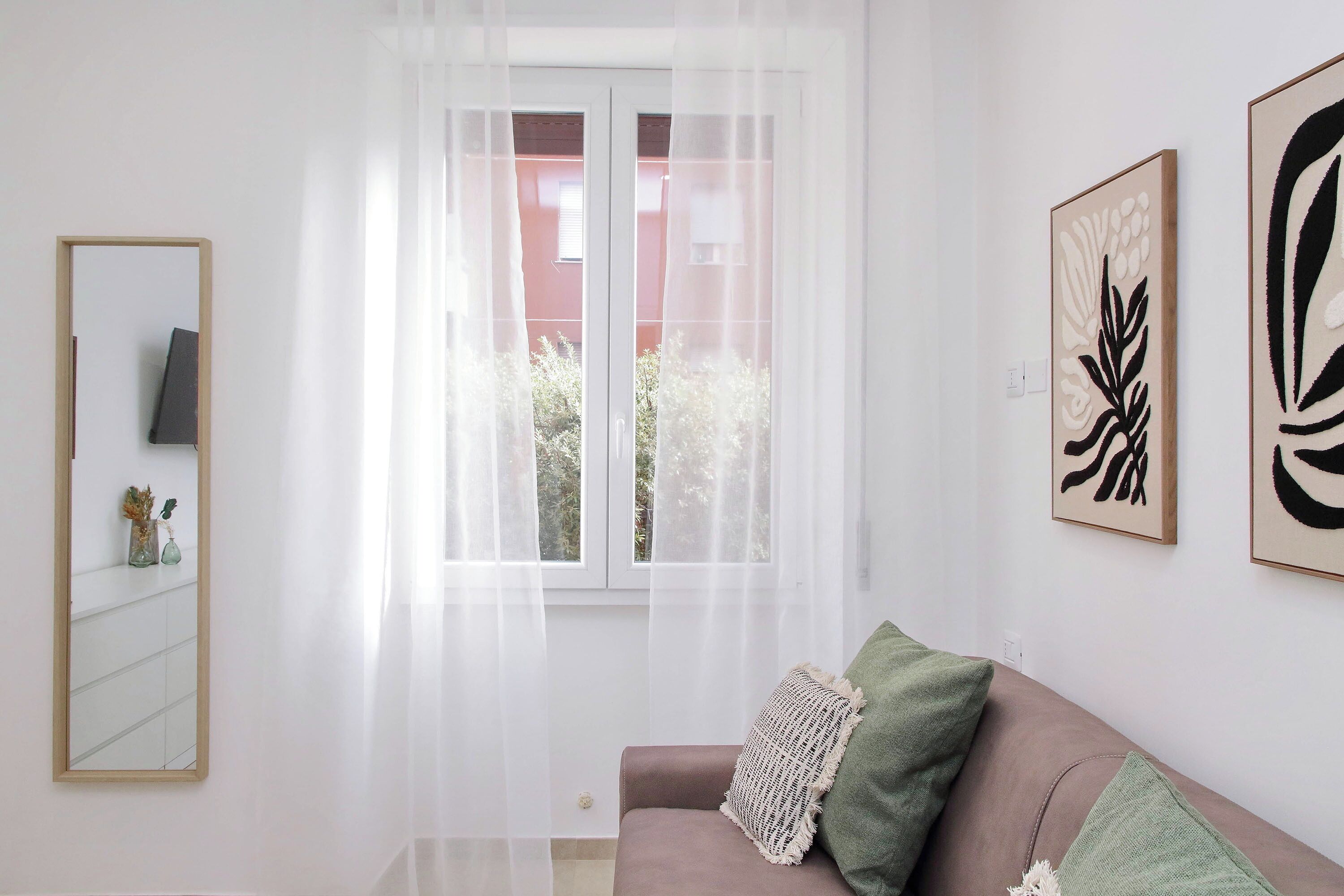 Une pièce avec une fenêtre, un miroir et deux œuvres d’art accrochées au mur.