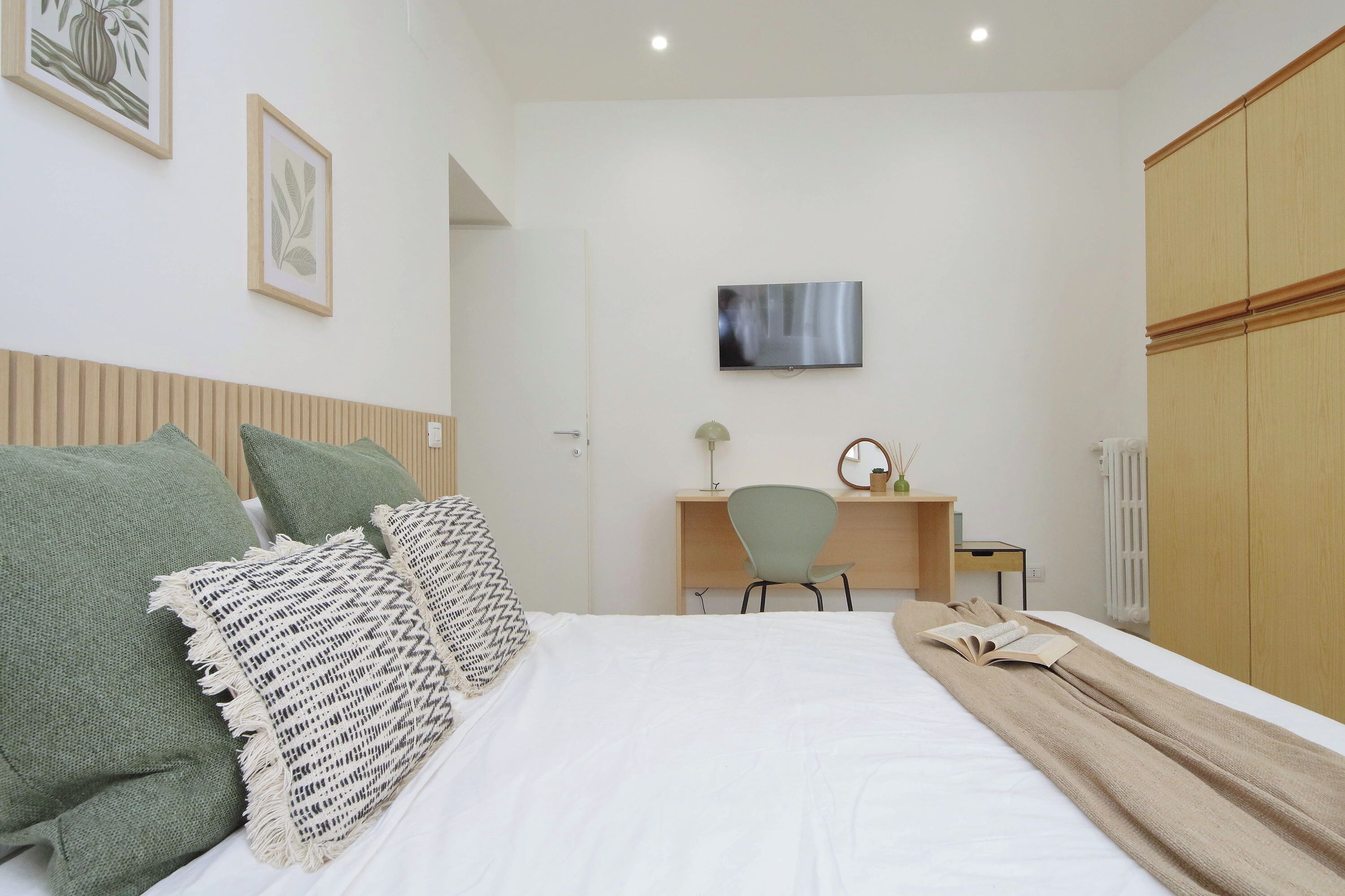 A bedroom with a bed, a desk, a chair, a TV, and a wardrobe.