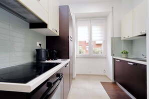 Eine moderne Küche mit einem schwarzen Herd, einer weißen Arbeitsplatte und dunklen Schränken. Ein Fenster mit Jalousien bietet Blick auf ein Gebäude.