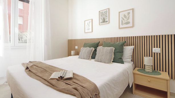 Ein ordentlich bezogenes Bett mit einer braunen Decke, einer Nachttischlampe und zwei gerahmten Pflanzenbildern an der Wand.