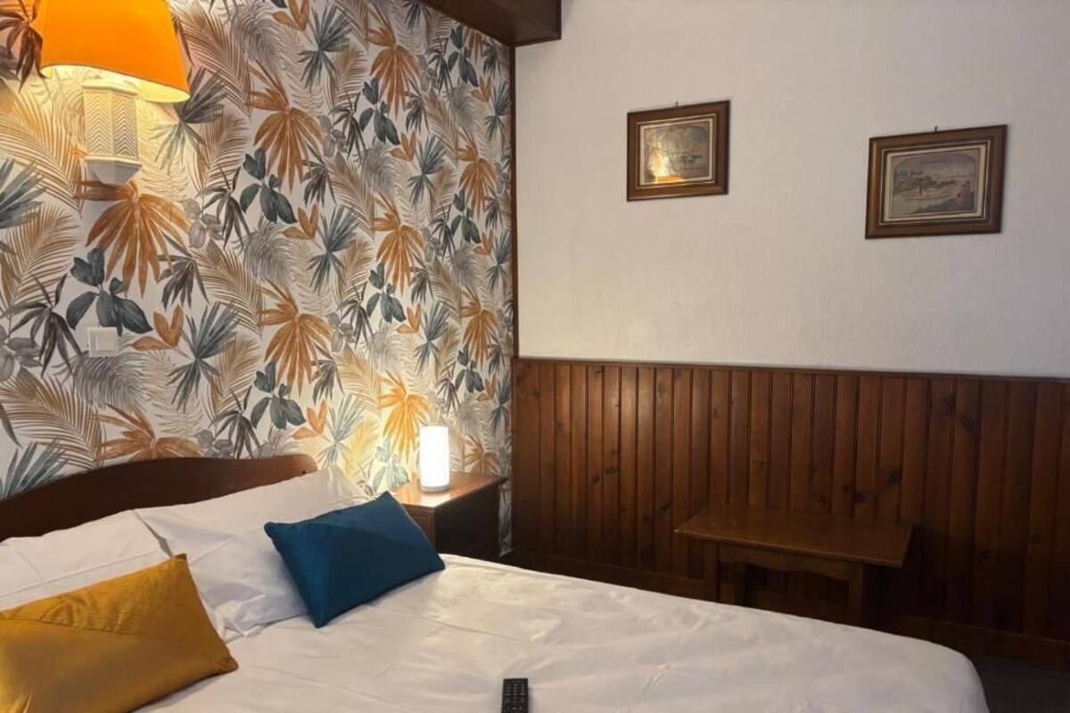 Una habitación de hotel con cama, mesita de noche, lámpara y un banco de madera.