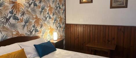 Una habitación de hotel con cama, mesita de noche, lámpara y un banco de madera.