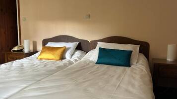 Una cama bien hecha con ropa blanca y dos almohadas, una amarilla y otra turquesa, en una habitación con cabecera y mesitas de noche de madera.