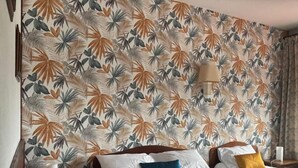 Hotellihuone, jossa on sänky, kaksi yöpöytää, lamppu ja kukkapainokuviollinen tapetti.