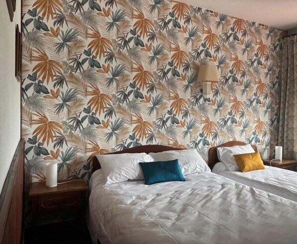 A hotel room with a bed, two bedside tables, a lamp, and a floral-patterned wallpaper. - Hôtel de Flandre (Compiègne)
