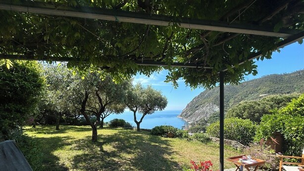 Un jardin agrémenté d’une pergola, d’un chemin de pierre, d’un espace salon extérieur et offrant une vue sur la mer et les collines.