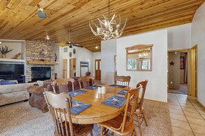 Un salon spacieux doté d’une cheminée, d’un plafond en bois et d’un coin repas avec une grande table et des chaises.