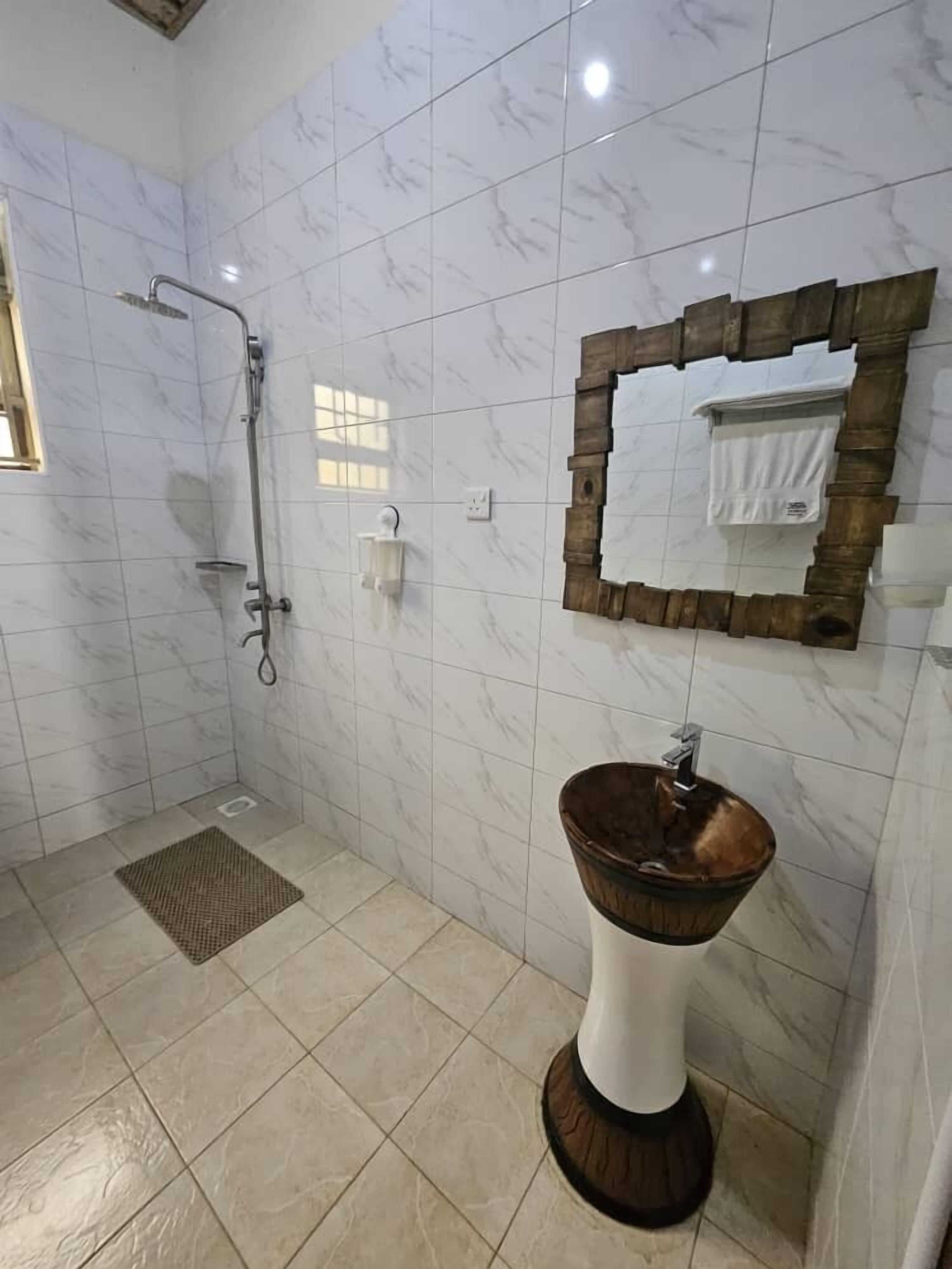 A bathroom with a shower, a sink with a wooden basin, and a mirror with a wooden frame.