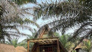 A small, rustic house with a thatched roof, surrounded by palm trees and a paved pathway leading to it. - Bugoma Palms Resort Beach and Hotel (Bugala Island)