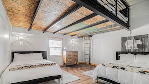 Un dormitorio con dos camas, piso de madera, techo abovedado y una lámpara fijada a la pared.