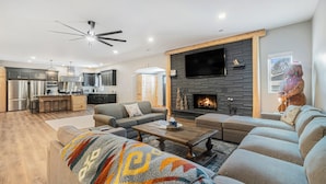 Una sala de estar moderna con chimenea, una cocina al fondo y un televisor grande montado en la pared.