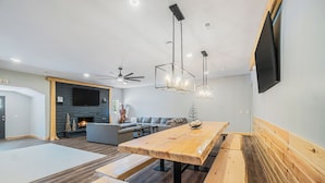 Una sala moderna con una mesa de comedor de madera, bancos, una chimenea, un sofá y un televisor de pantalla plana montado en la pared.