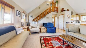 A spacious living room with a high ceiling, a wooden staircase, a sofa, a blue armchair, and a coffee table. - Panoramic Views! 'The Cozy Fox Cabin' in Livermore (Livermore)