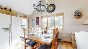 A dining area with a wooden table set for four, surrounded by chairs. A chandelier hangs from the ceiling, and a clock is visible on the wall. - Panoramic Views! 'The Cozy Fox Cabin' in Livermore (Livermore)
