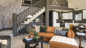A spacious living area with a high ceiling, a staircase, a kitchen, and a dining area. - Luxe Mtn Cabin | Hot Tub, Sauna, Stargazing Dome (Bailey)