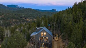 A cabin with a large porch, a staircase leading to the entrance, and a view of the surrounding forest and mountains. - Luxe Mtn Cabin | Hot Tub, Sauna, Stargazing Dome (Bailey)