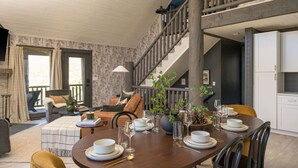 A dining area with a wooden table set for four, a staircase, and a living room with a sofa and a fireplace. - Luxe Mtn Cabin | Hot Tub, Sauna, Stargazing Dome (Bailey)