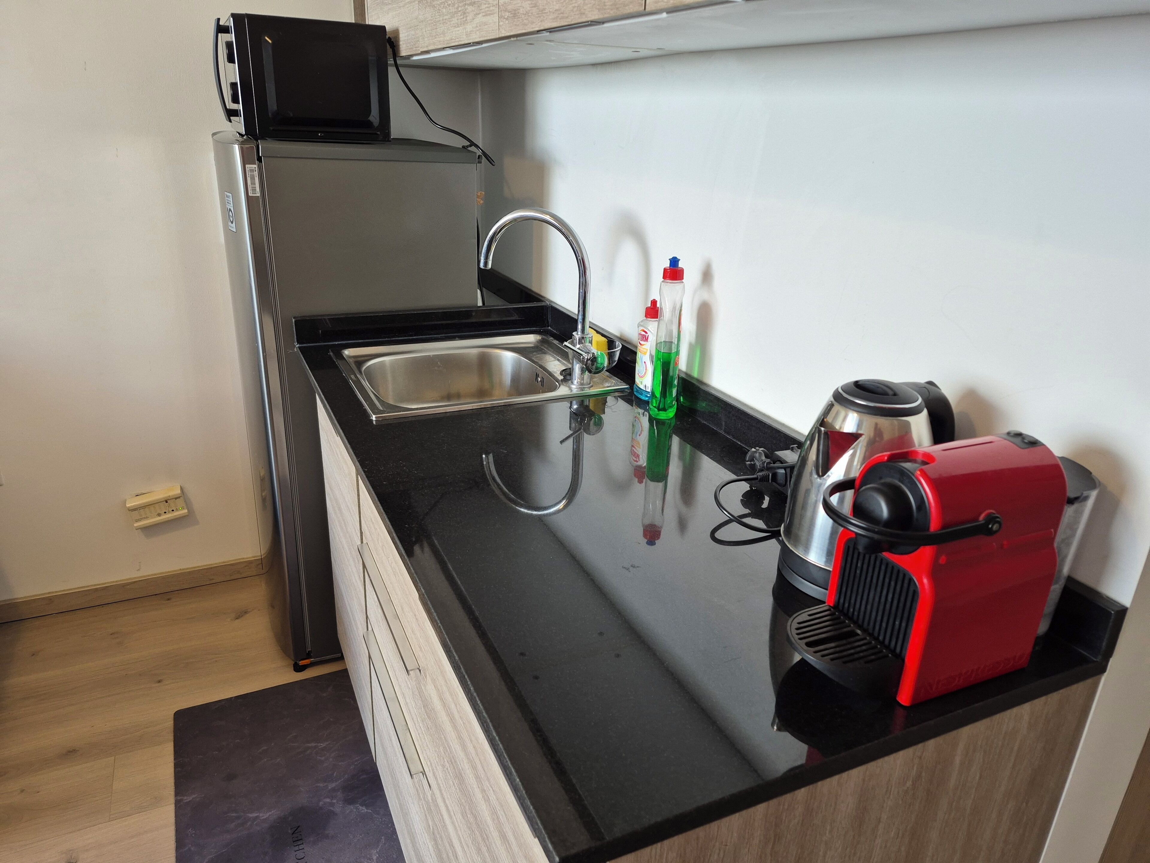A compact kitchen with a stainless steel sink, a microwave, and a red coffee maker on the counter.