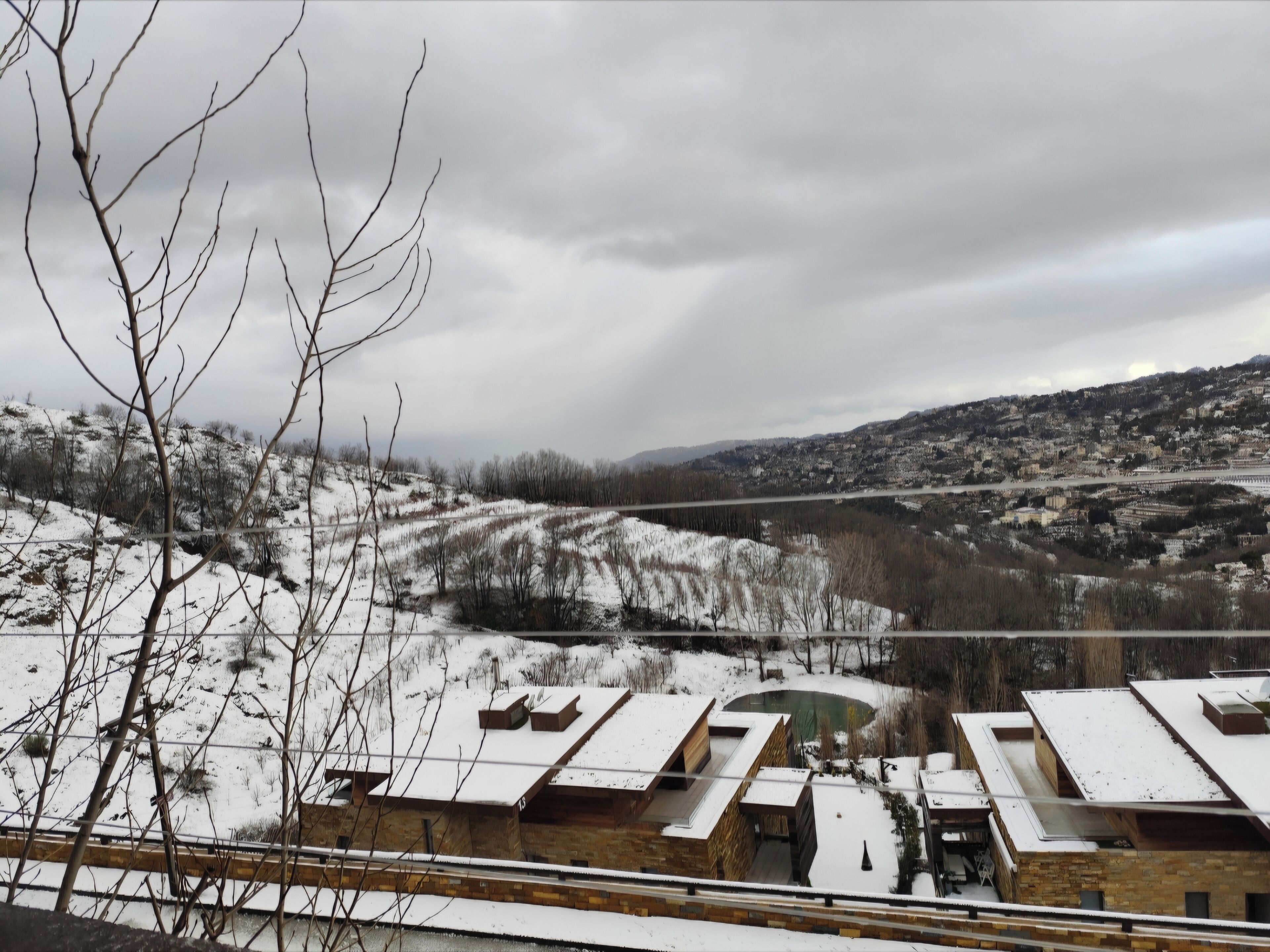 Un edificio moderno con techo plano y una ventana grande, rodeado de nieve y árboles.