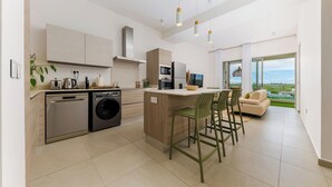 A modern kitchen with built-in appliances, a central island, and a dining area with chairs. - TROPICA BLISS (Grand Baie)