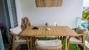 Een houten tafel met witte kussens, een geweven hanglamp en uitzicht op de stad vanaf een balkon.