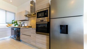 A modern kitchen with stainless steel appliances, wooden cabinetry, and a built-in dishwasher. - TROPICA BLISS (Grand Baie)