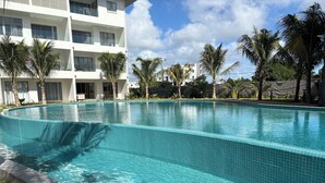 A swimming pool with tiled edges, surrounded by palm trees and a multi-story building with balconies. - TROPICA BLISS (Grand Baie)
