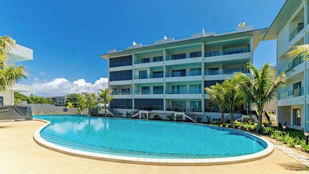 A modern hotel with a large pool, multiple balconies, and palm trees. - TROPICA BLISS (Grand Baie)