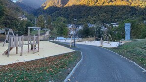 A playground with swings and climbing structures, a paved path, and a mountain in the background. - Apartment T2 Vu mountain 700 meters cable car swimming pool in summer (Cauterets)